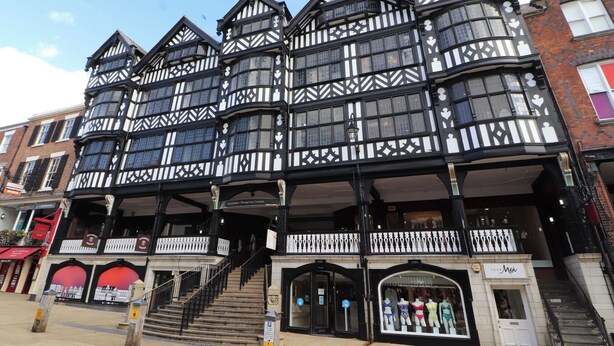 A traditional black and white timber-framed building with multiple floors, a central staircase, and a ground-level entrance with a shop on the right. - Kingsley Loft (Chester)