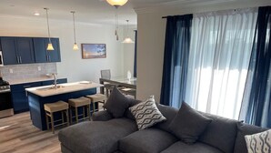 Una sala moderna con un sofá gris, una pequeña mesa redonda de centro y una cocina al fondo.