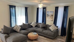 Una sala de estar con un sofá modular, un otoman redondos y un ventilador de techo.