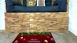 Un coin salon accueillant, avec un mur en bois et des sièges rembourrés. Un tapis aux motifs festifs sur le thème de Noël est posé sur le sol.