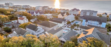 Zona residencial costera con casas, una piscina y un atardecer sobre el océano.