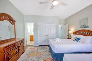 Quarto com cama, cómoda, ventoinha no teto e porta que dá para outro espaço.