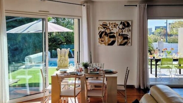 A modern living room with a large sliding glass door leading to a patio area. There is a dining table with chairs and a sofa in the room. - VILLA La Mazal, Bord de Mer, Balnéo, Piscine Clim (Sète)
