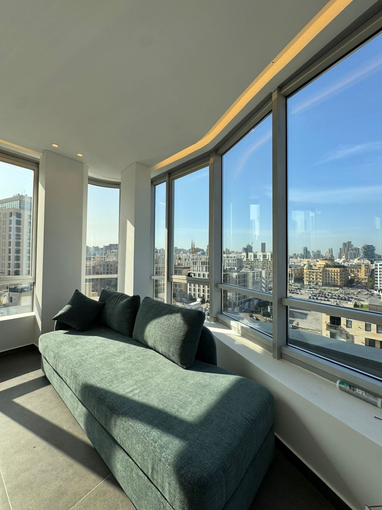 Un salón moderno con sofá verde, ventanas amplias y vistas a la ciudad.