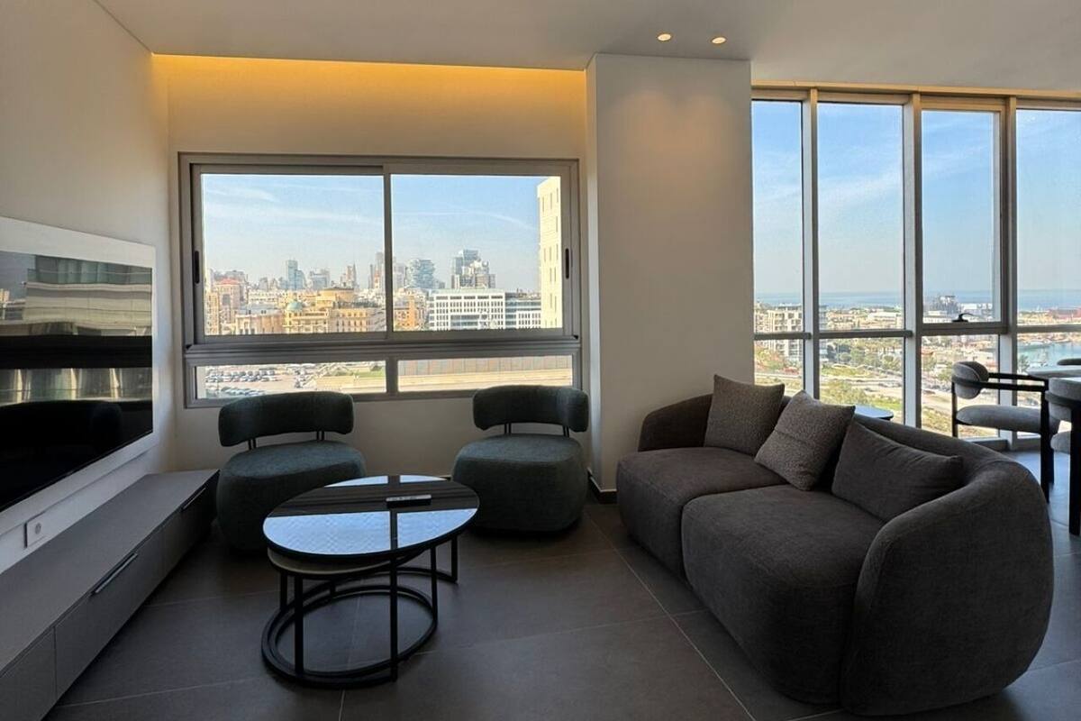 A modern living room with a large window, a sofa, a small table, and a TV.