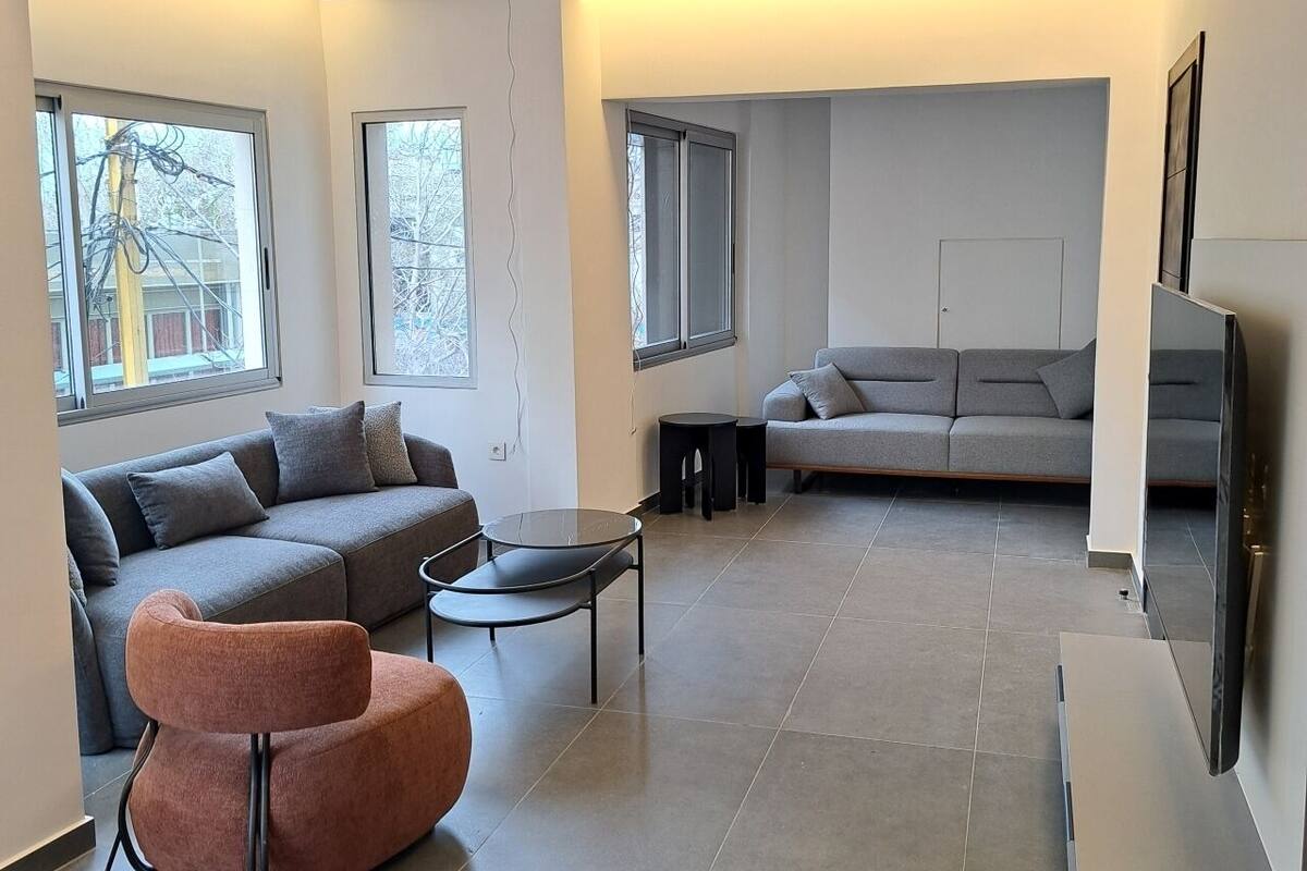 A modern living room with a grey sectional sofa, a round orange chair, a glass coffee table, and a flat-screen TV.