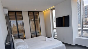Un dormitorio moderno con una cama grande, un televisor en la pared y vistas a la ciudad desde la ventana.