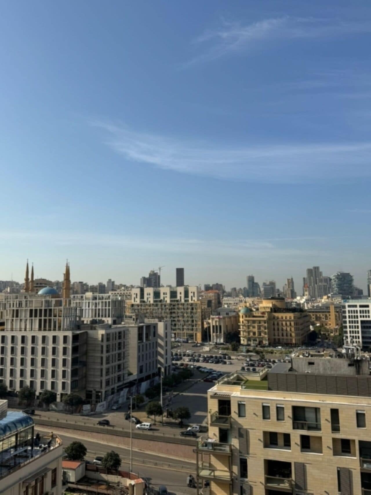 A cityscape with modern buildings, a mosque with a dome and minarets, and a parking lot.