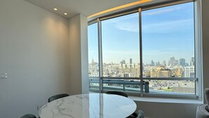 Un comedor moderno con una mesa redonda y cuatro sillas, ventanas amplias con vistas a la ciudad y un diseño interior limpio y minimalista.