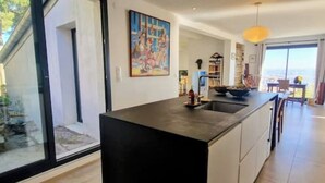 A modern kitchen with a black countertop, a painting on the wall, and a view of the outdoors. - VILLA des Rêves, Superbe Vue, Swimming Pool, Prox center (Sète)
