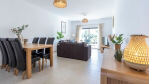 Een moderne woonkamer met een eethoek, met een bank, een houten eettafel met stoelen en een groot raam met gordijnen.