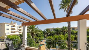 Een balkon met een houten pergola, een gedekte tafel met borden en glazen, en een stoel.
