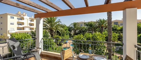 A balcony with a wooden pergola, a table set with plates and glasses, and a chair.