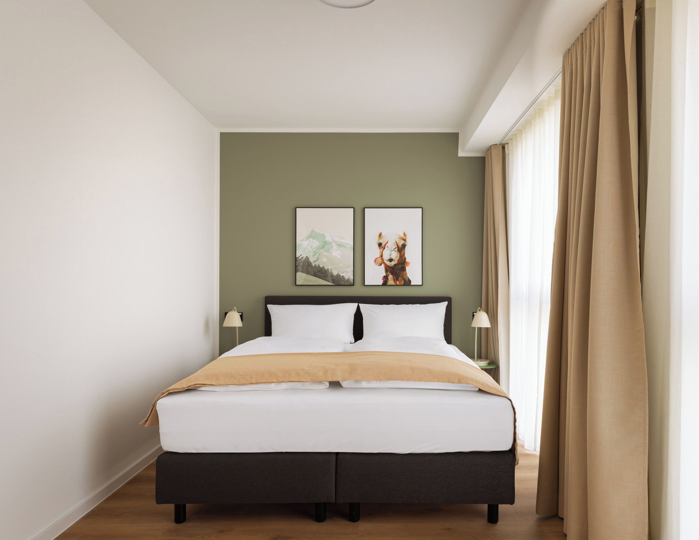A bedroom with a bed, two wall-mounted lamps, and two framed pictures.