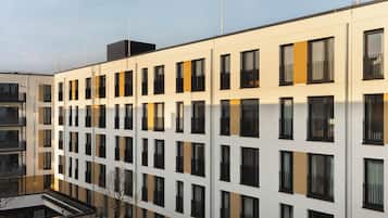 Ein modernes, mehrgeschossiges Gebäude mit einer symmetrischen Fassade, das regelmäßig angeordnete Fenster und Balkone aufweist.