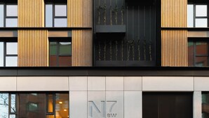 A modern building facade with vertical wooden slats, a black vertical panel with plants, and a sign with "NZ" and "ew" indicating the name. - Limehome Mannheim City Center (Mannheim)