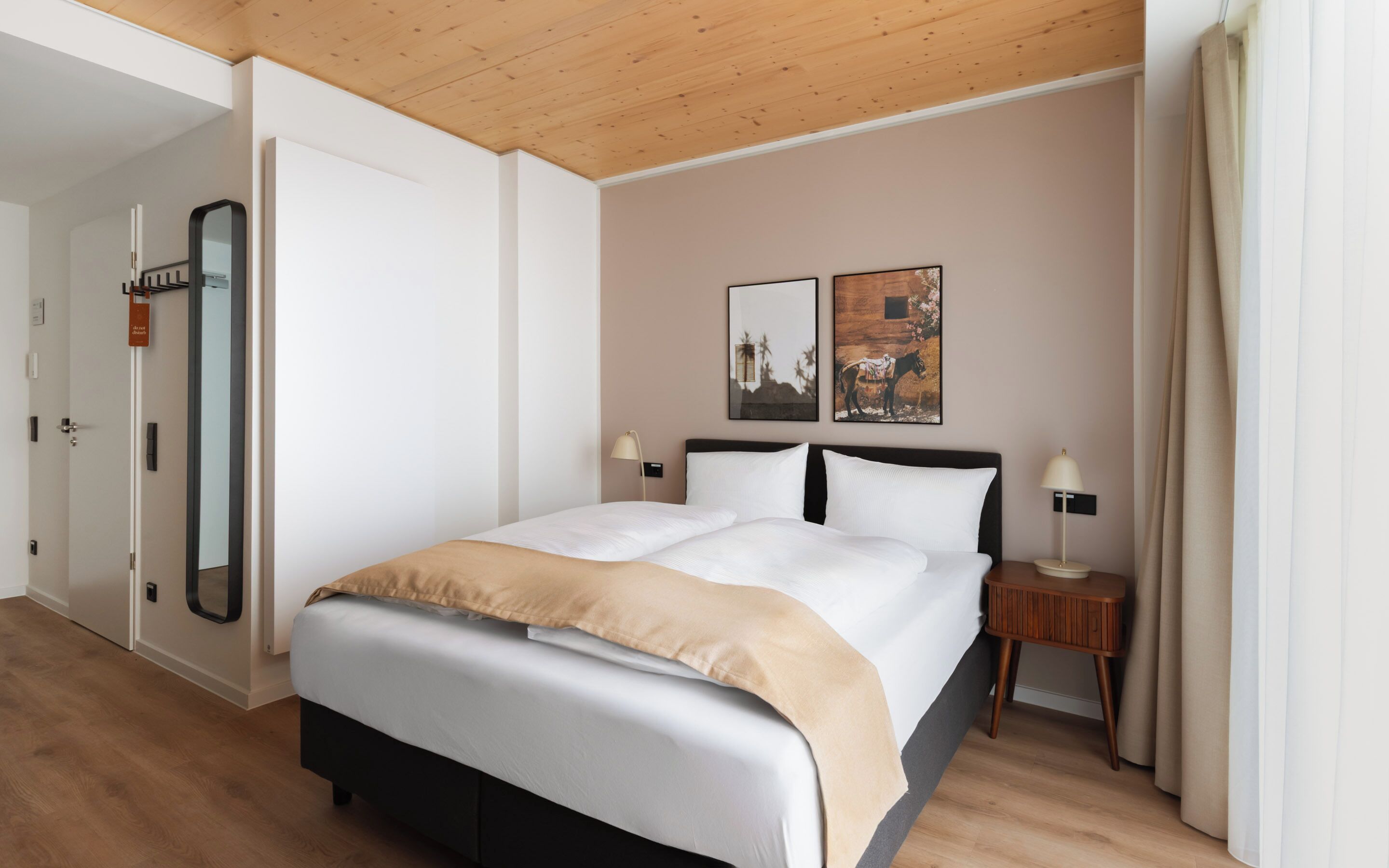 Ein Hotelzimmer mit einem großen Bett, zwei Nachttischen, einem Spiegel und Bildern an der Wand.