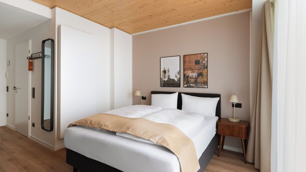 A hotel room with a large bed, two bedside tables, a mirror, and artwork on the wall. - Limehome Mannheim City Center (Mannheim)