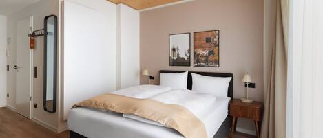 A hotel room with a large bed, two bedside tables, a mirror, and artwork on the wall.