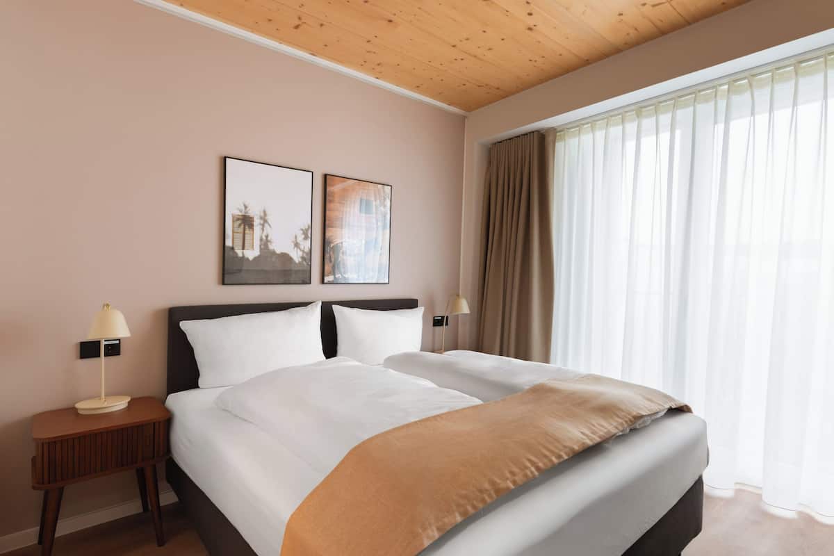 Habitació d'hotel amb un llit gran, dues taules de nit, un capçal de llit i una finestra amb cortines.