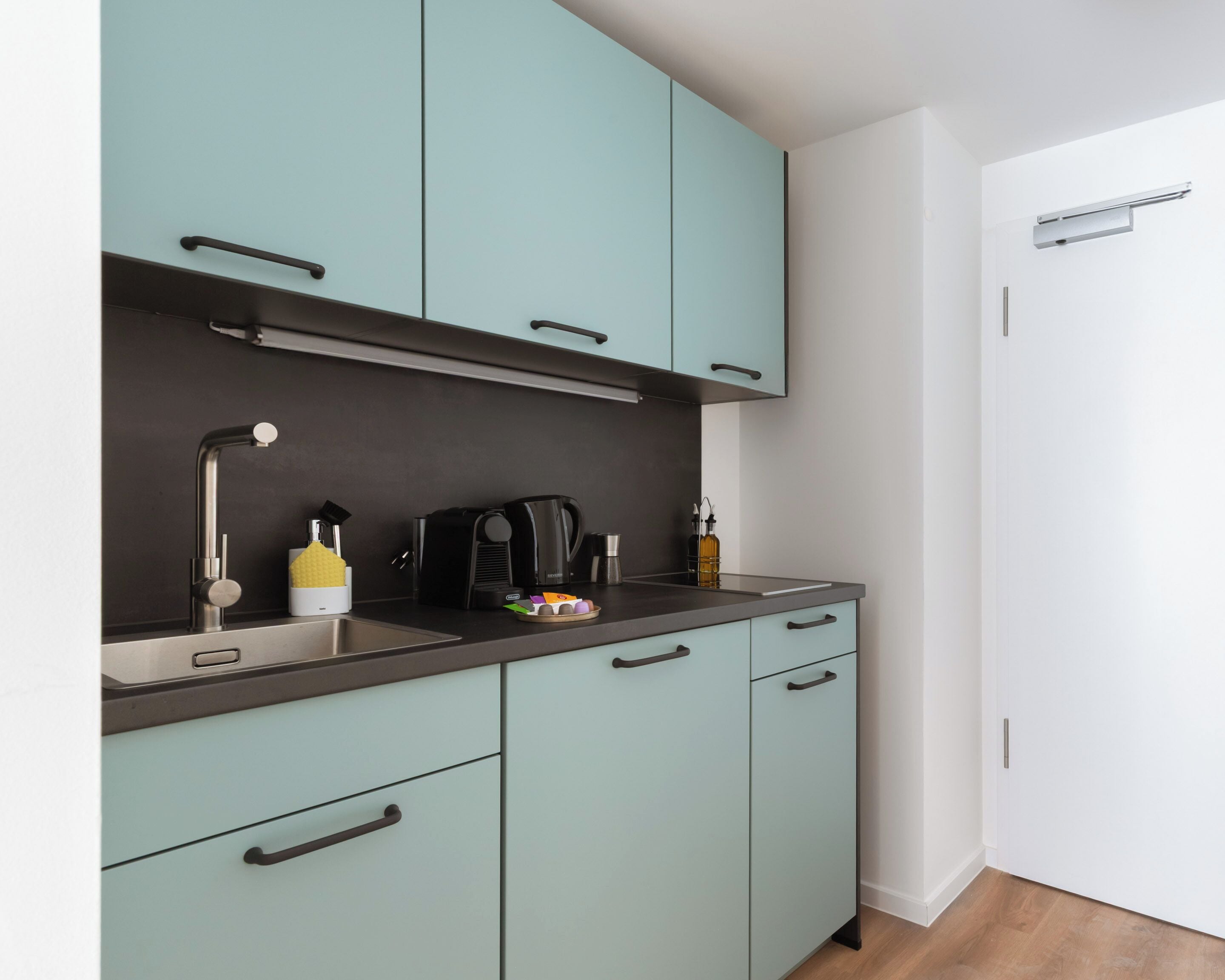 A modern kitchen with teal cabinets, a stainless steel sink, and a coffee maker.