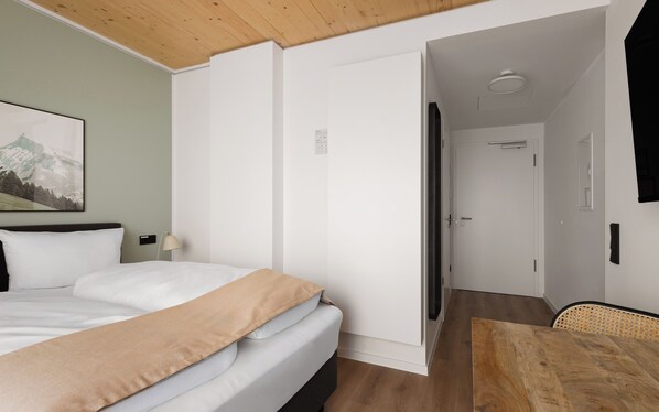 A hotel room with a bed, a wooden ceiling, a painting on the wall, and a door leading to another room.