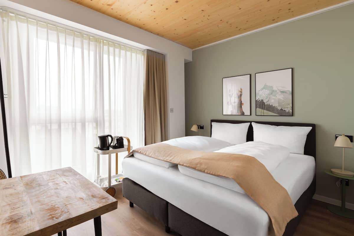 Una habitació d'hotel amb un llit, una taula, una cafetera i dos quadres penjats a la paret.