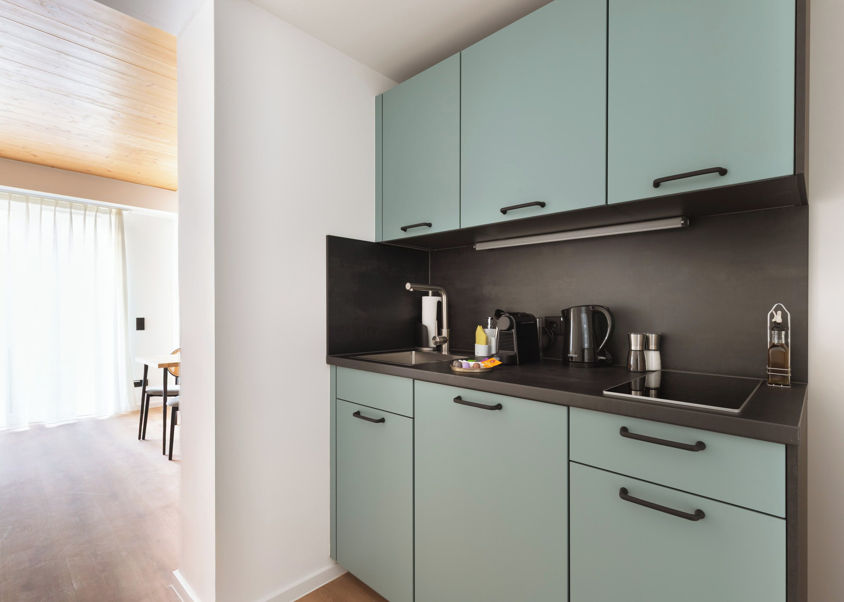 A modern kitchen with teal cabinets, a black countertop, and stainless steel appliances.