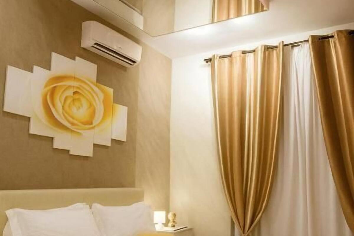A bedroom with a bed, a wall-mounted air conditioner, and a large window with curtains.