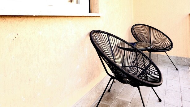Two black wireframe chairs on a tiled patio with a yellow wall and a window. - Bed Cinecittadue (Rome)