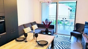 Une cuisine moderne avec des meubles de couleur sombre, un coin repas avec une table en bois dressée pour deux personnes, et un balcon agrémenté de mobilier d’extérieur.