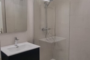 A modern bathroom with a white sink, a mirror, and a glass-enclosed shower area. - Le Neuburg Sur La plage Vue Mer Clim Piscine (Sète)