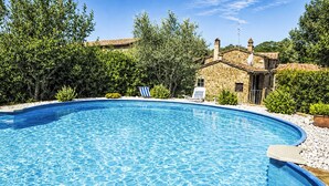 A swimming pool with clear blue water, surrounded by greenery and a stone building with a tiled roof. - Il Cottage Roccaio by Interhome (Castiglion Fiorentino)