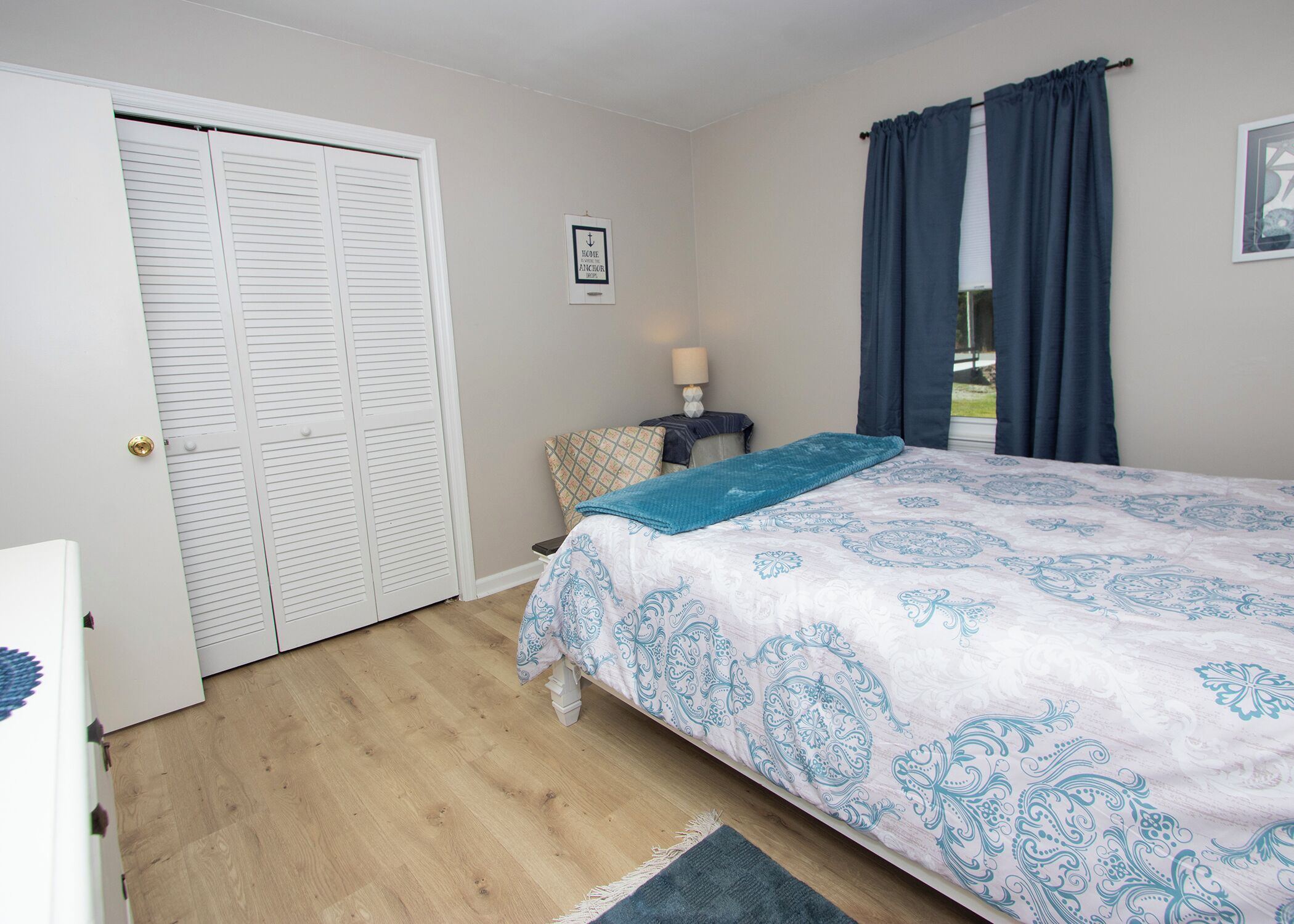 Un dormitorio con cama, mesita de noche, lámpara, ventana con cortinas y puerta con persianas.