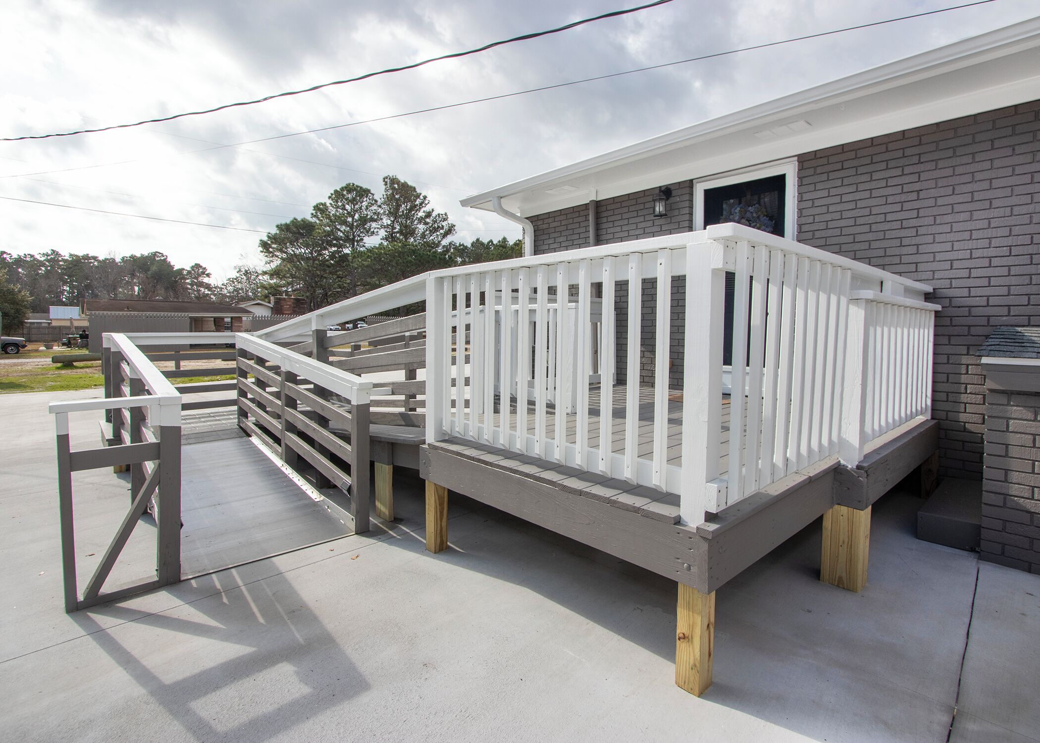 A wooden deck with a white railing, attached to a building with a brick exterior.
