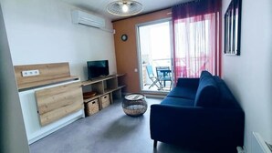 En moderne stue med blå sofa, fjernsyn, træskabe og en skydedør til et udendørs område.