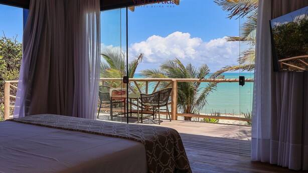 Een slaapkamer met een groot bed, uitzicht op het strand en een balkon met stoelen en een tafel.