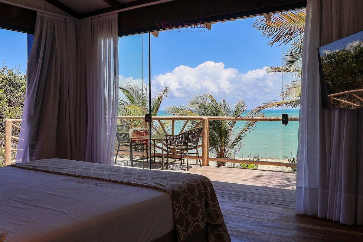 A bedroom with a large bed, a view of the beach, and a balcony with chairs and a table.