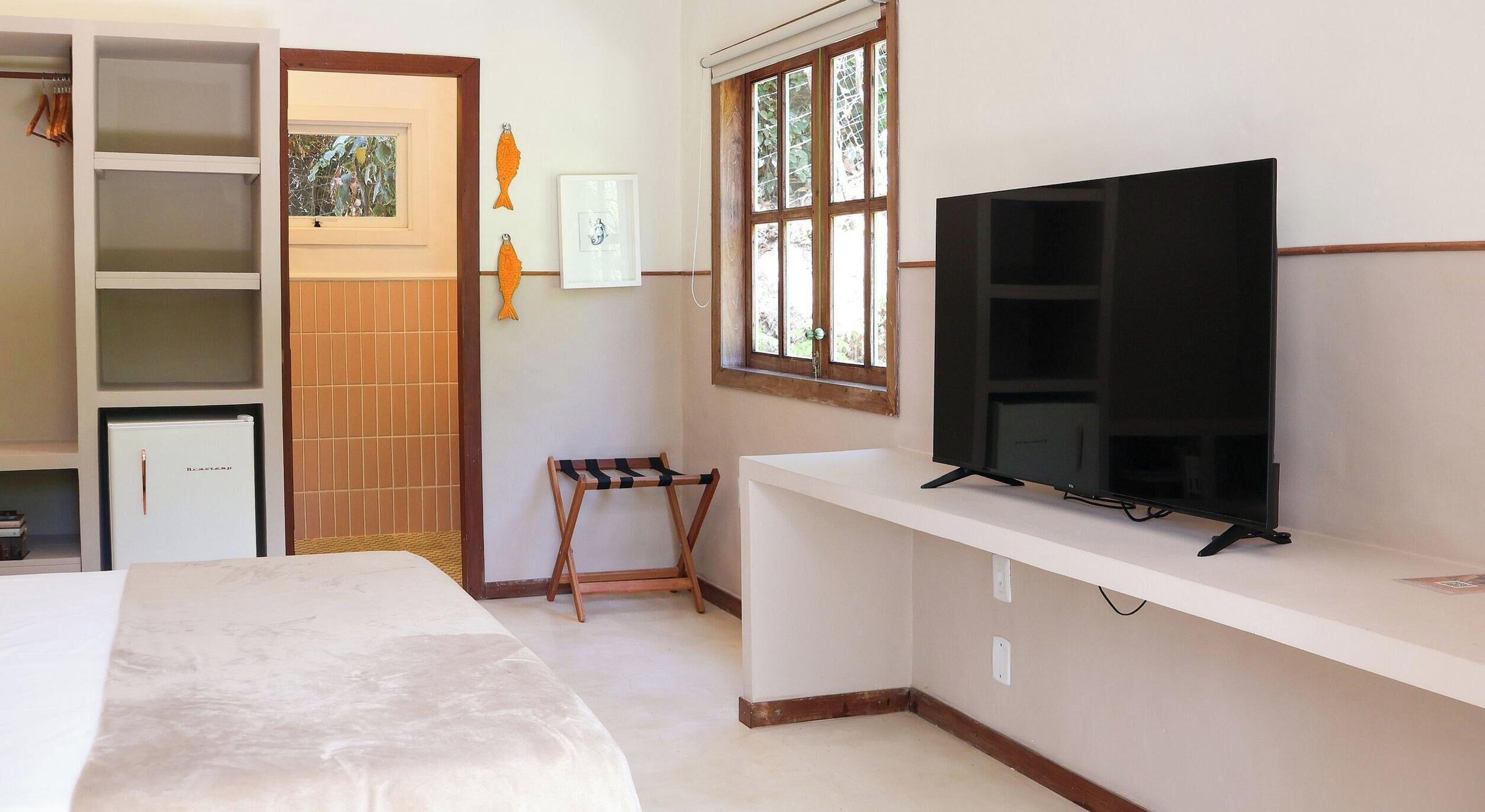 A hotel room with a bed, a TV on a stand, a wardrobe, and a window with a view of greenery.