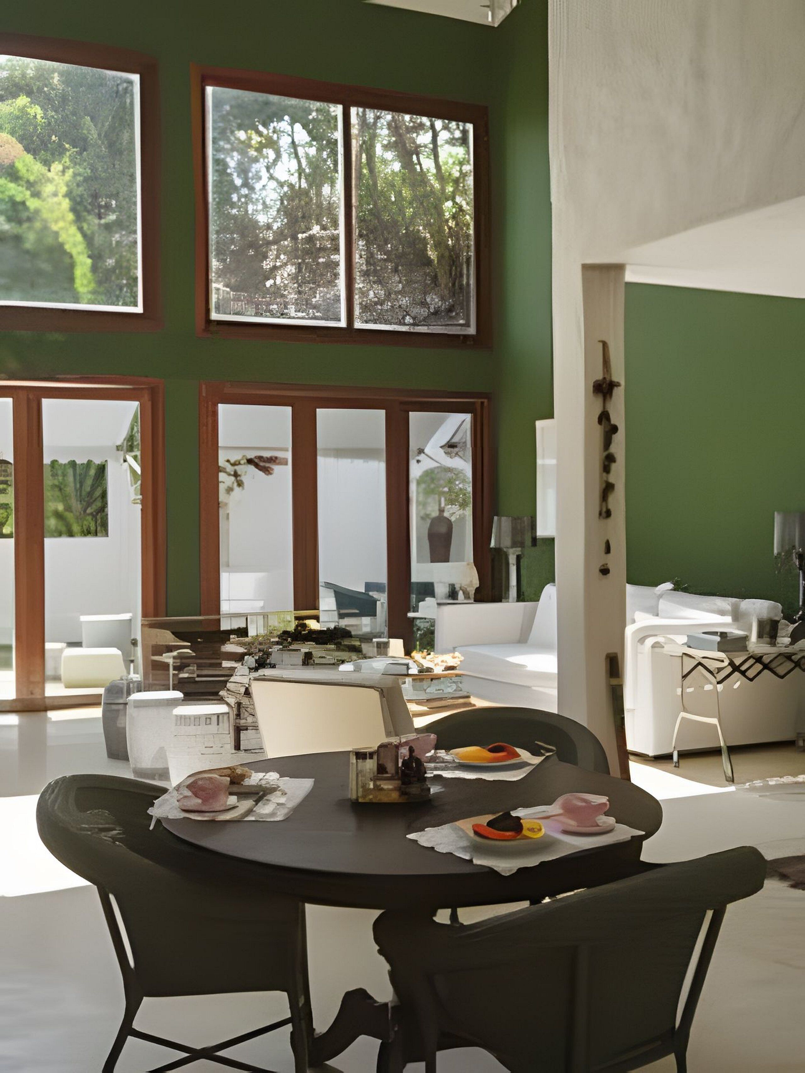 Uma área de refeições com uma mesa posta para dois, janelas amplas e vista para o verde lá fora.