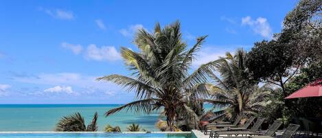 A poolside area with lounge chairs and palm trees, overlooking a clear blue ocean.