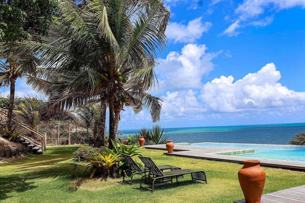 A poolside area with a view of the ocean, palm trees, and a wooden deck.