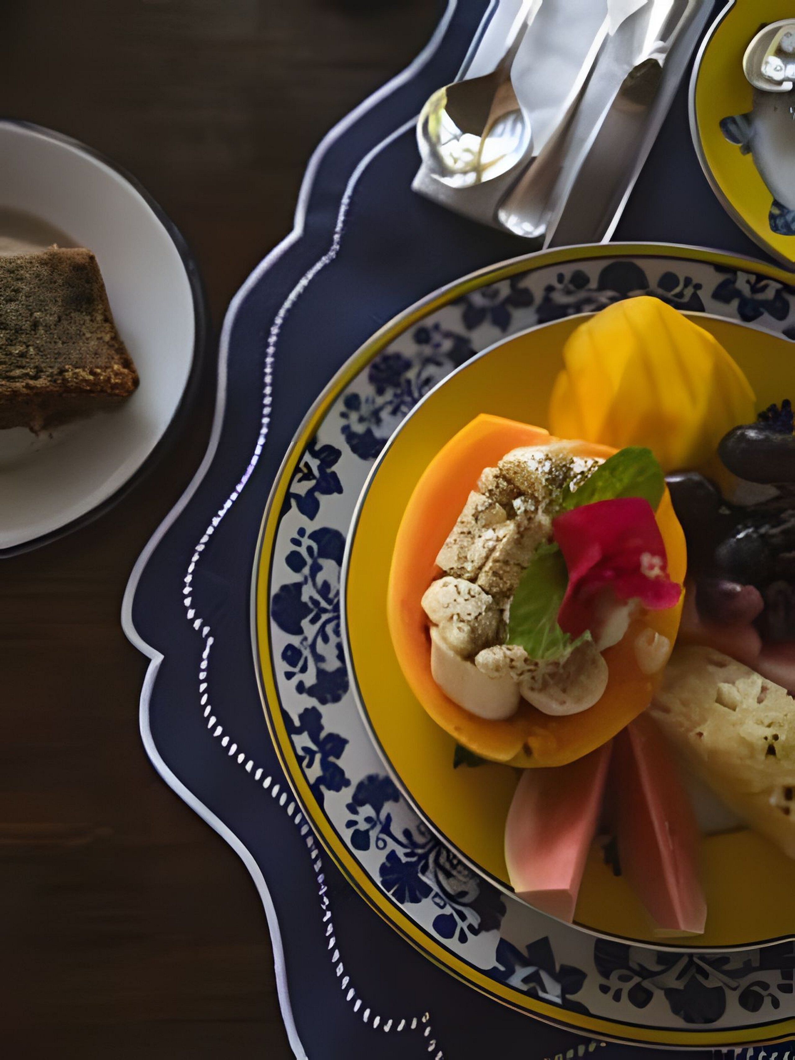A table setting with a plate of food, including a slice of bread, a yellow bowl with a decorative item, and a spoon.