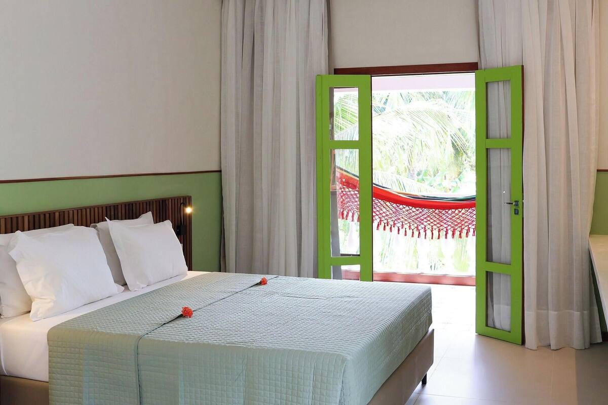 A hotel room with a bed, a green-framed door, and a view of a red-roofed structure outside.