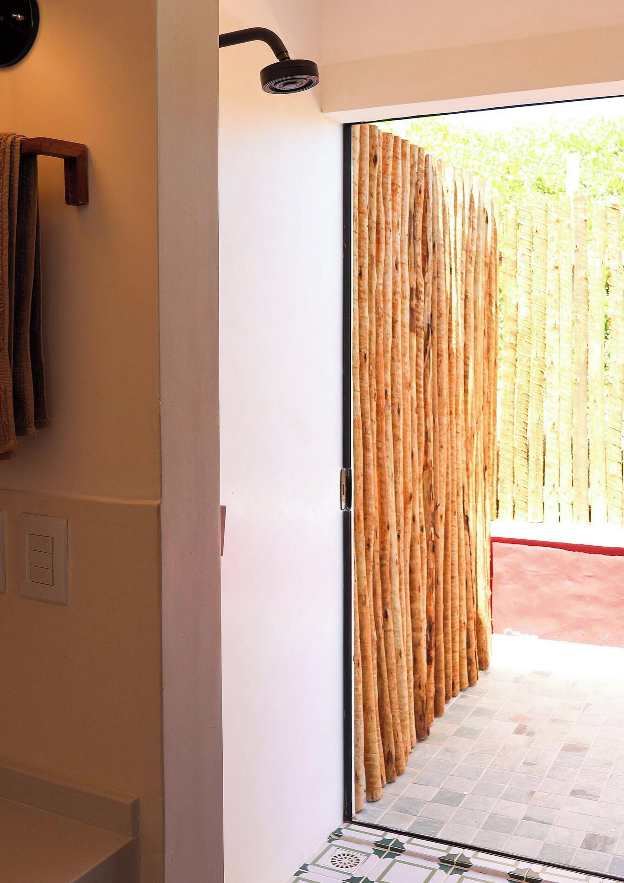 A bathroom with a shower, a towel rack, and a door leading to an outdoor area with a bamboo fence.