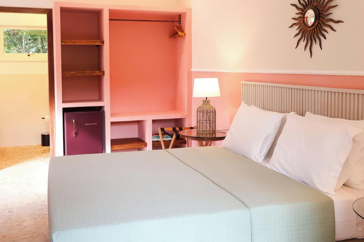A hotel room with a bed, a desk with a lamp, a wardrobe, and a sun-shaped wall decoration.