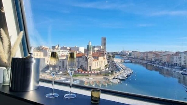 A view from a window overlooking a river with buildings and a tall tower. - Le Tassigny Duplex Superbe Vue sur les Quai Centre (Sète)