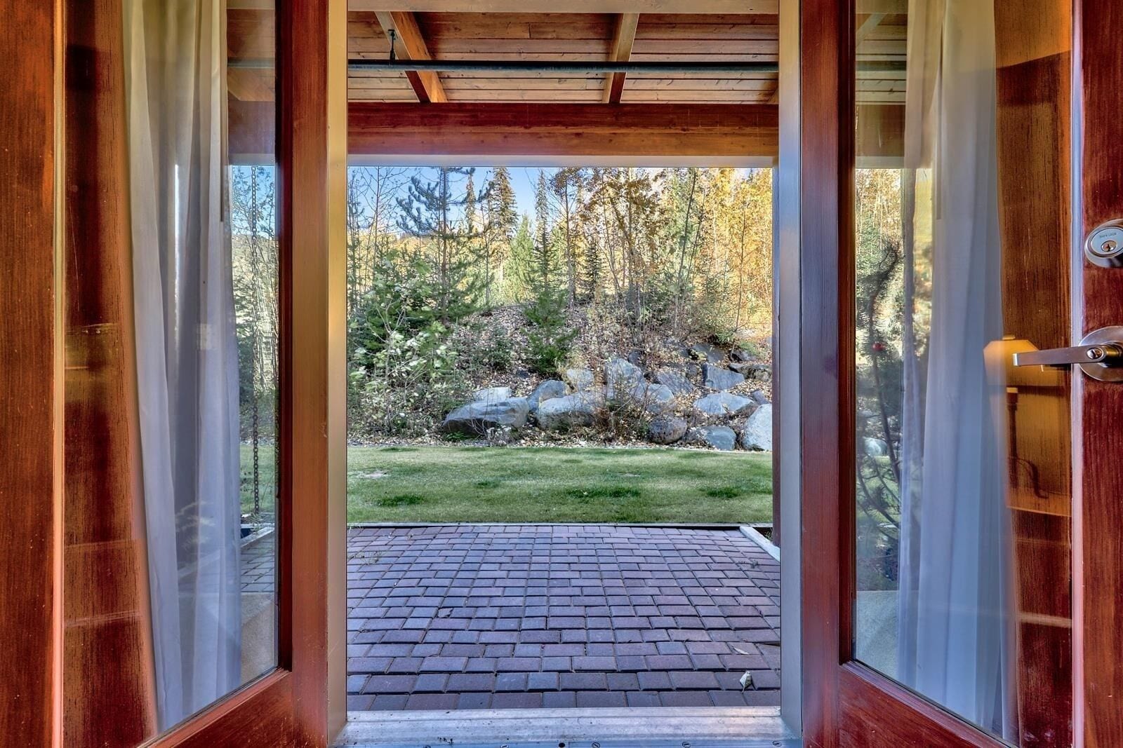 A wooden door leading to a paved outdoor area with a view of a forested landscape.