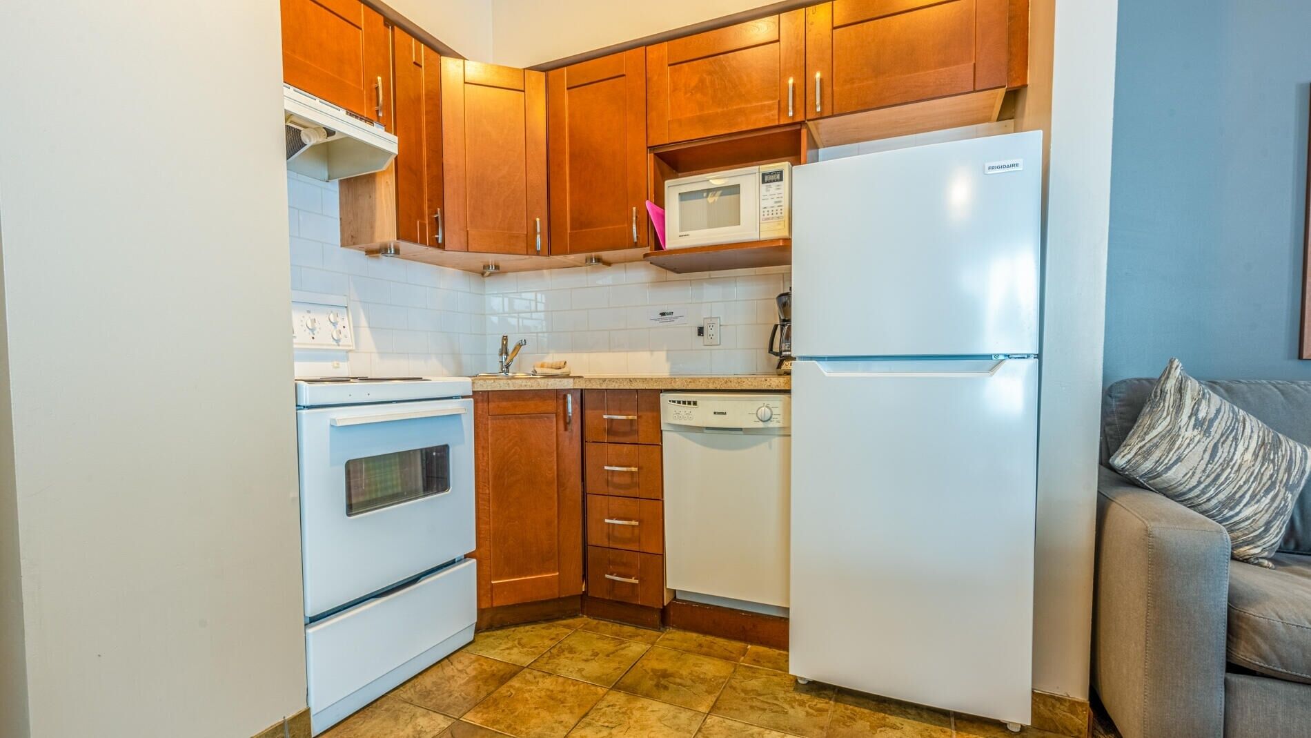 A compact kitchen with wooden cabinets, a white refrigerator, a microwave, a stove, and a dishwasher.