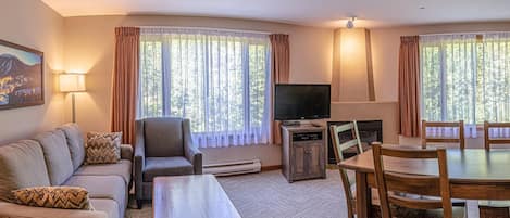 Un salon chaleureux avec un canapé, un fauteuil, une télévision, une cheminée et une table à manger.